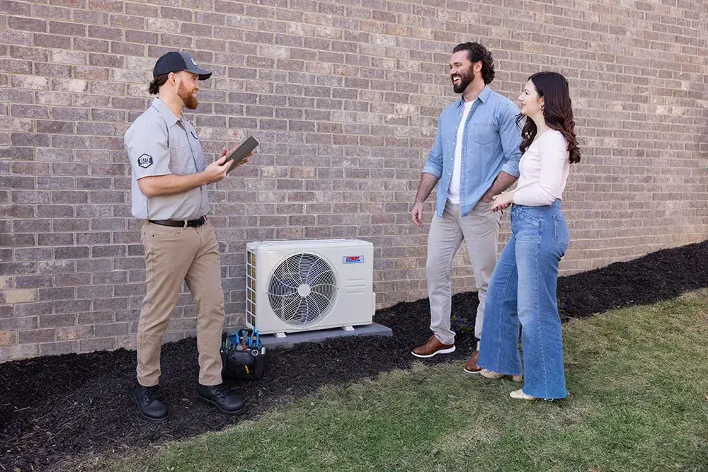 HVAC technician reviewing a new outdoor heat pump installation with homeowners